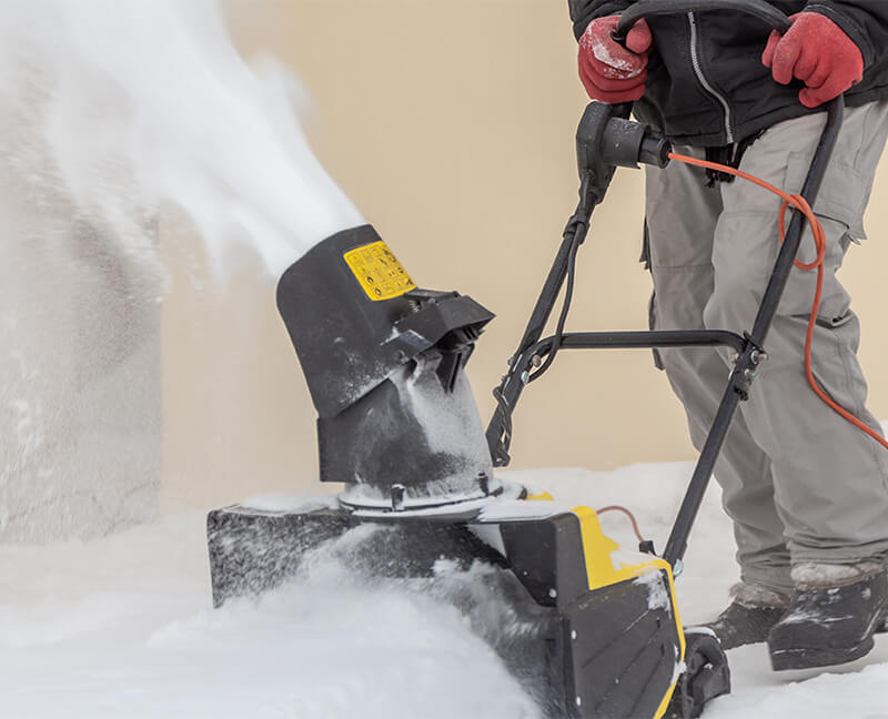 Man operating a snowblower in winter weather.